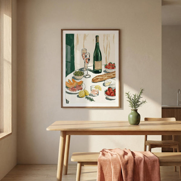 Framed artwork of a table setting with food and wine on a wall above a wooden dining table.
