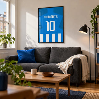 Football Shirt Poster in Blue and White Stripes with Blue Sleeves, framed on the wall of a compact modern living room in a football fan's first UK flat (22-28) with a warm white wall and oak floor