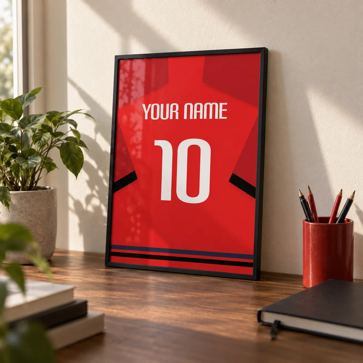 Football Shirt Poster in Red with Black Sleeve Bands, a small A4 framed print leaning on a walnut desk