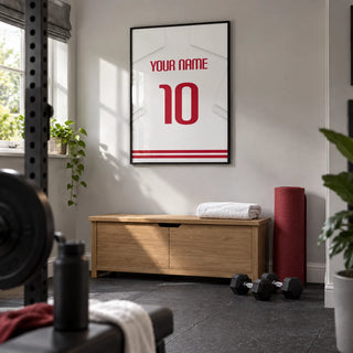 Football Shirt Poster in White with Red Number, framed on the wall of a compact home gym in a converted UK spare room with light grey walls and dark rubber flooring