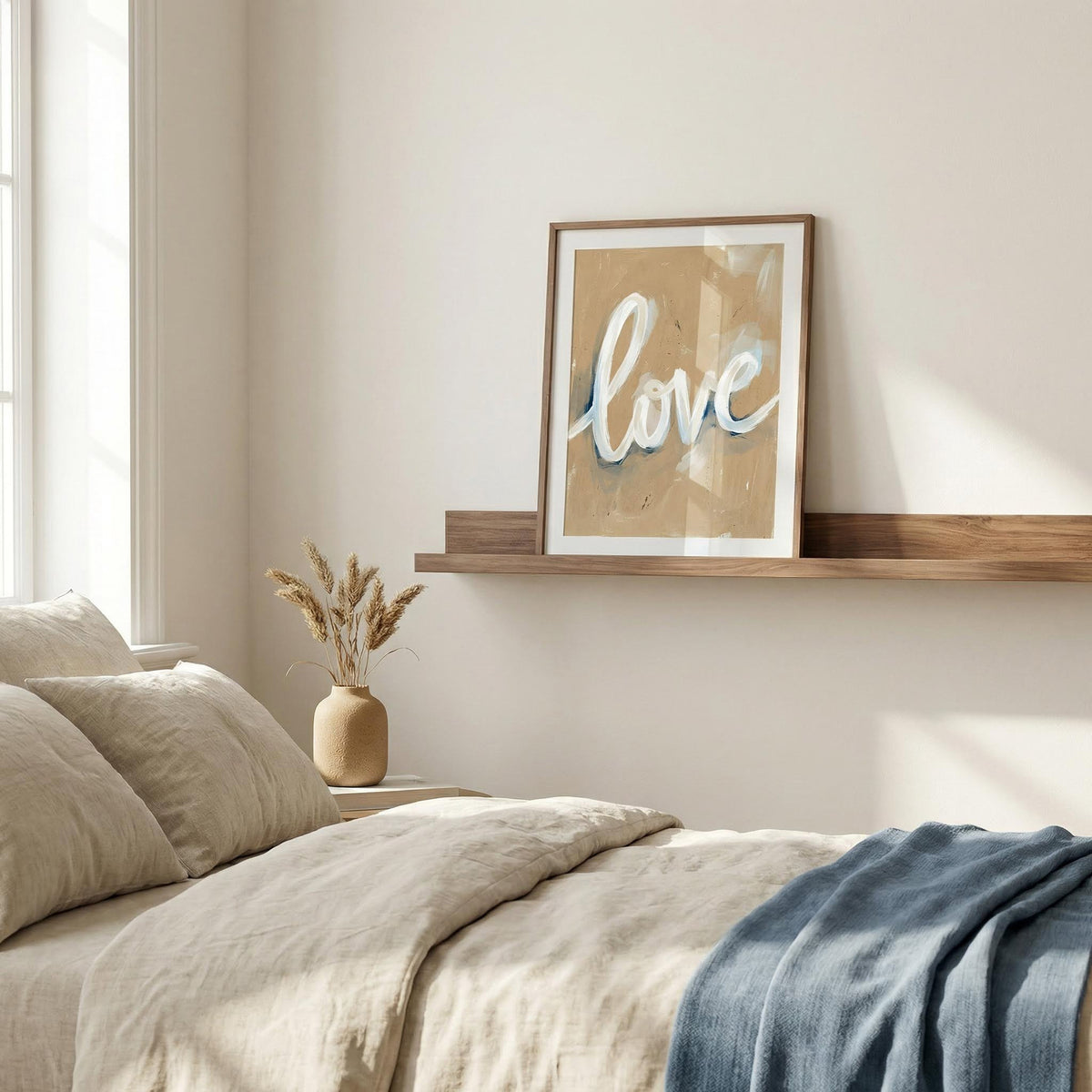 Neatly made bed with pillows and a blanket, framed 'love' picture on the wall.