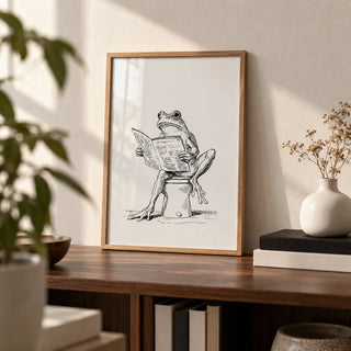Reading Frog Art Print, a small A4 framed print leaning on a walnut bookshelf in a living room
