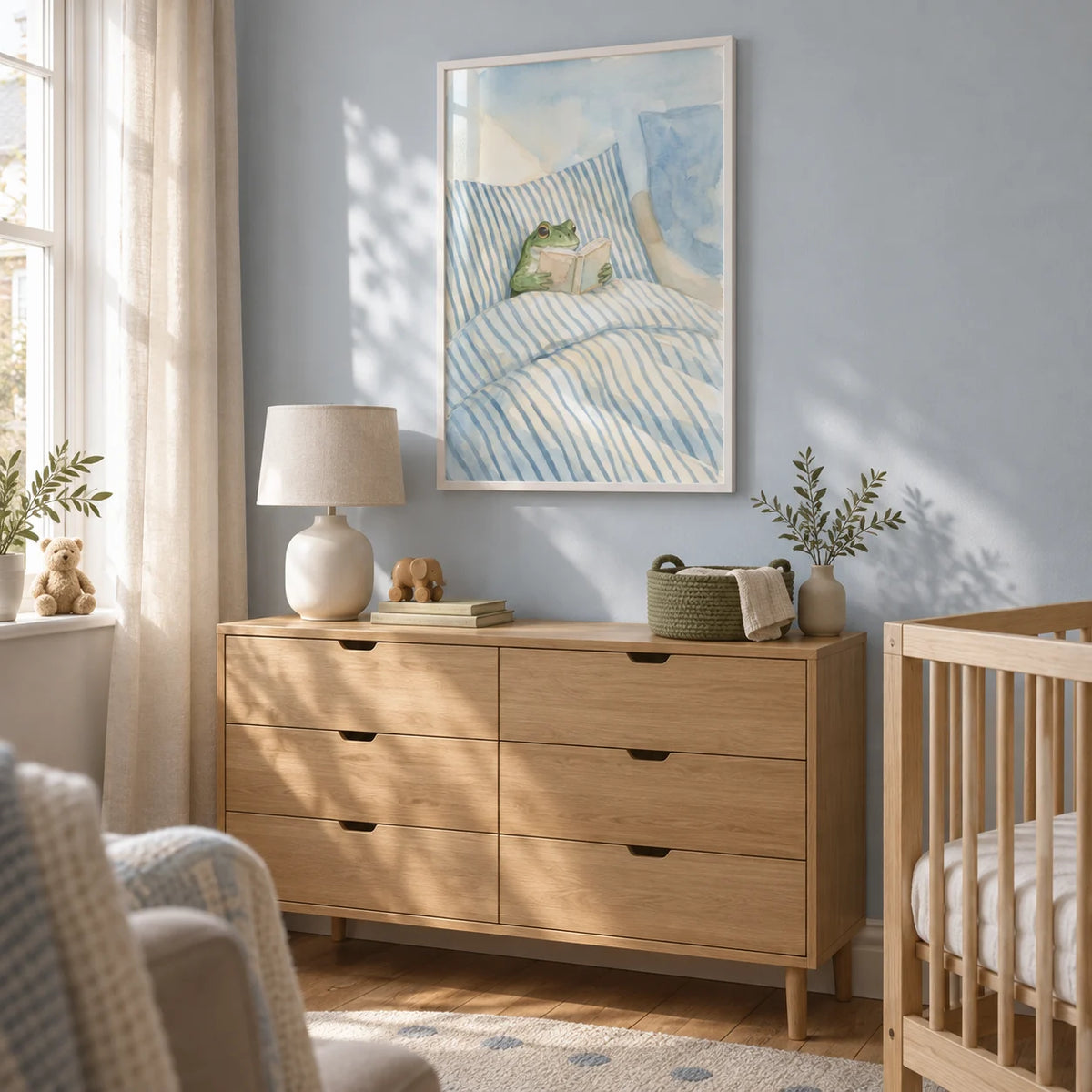 Frog Reading In Bed Print, framed on the wall of a calm nursery in a UK terraced house with a pale blue wall and natural wood furniture