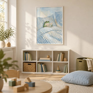 Frog Reading In Bed Print, framed on the wall of a quiet family playroom with a cream wall and pale timber floor in a UK home