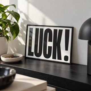 Good Luck Print, a small A4 framed print leaning on a black shelf in a living room