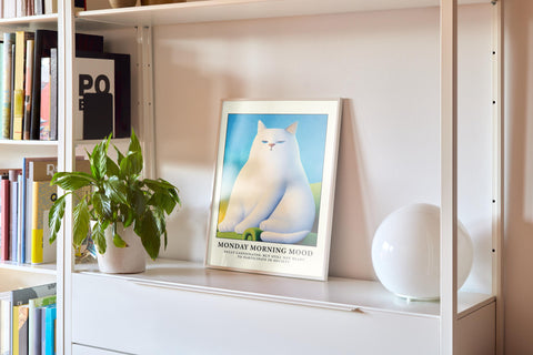 Grumpy white cat sitting on a couch with a funny caption about Monday mornings.