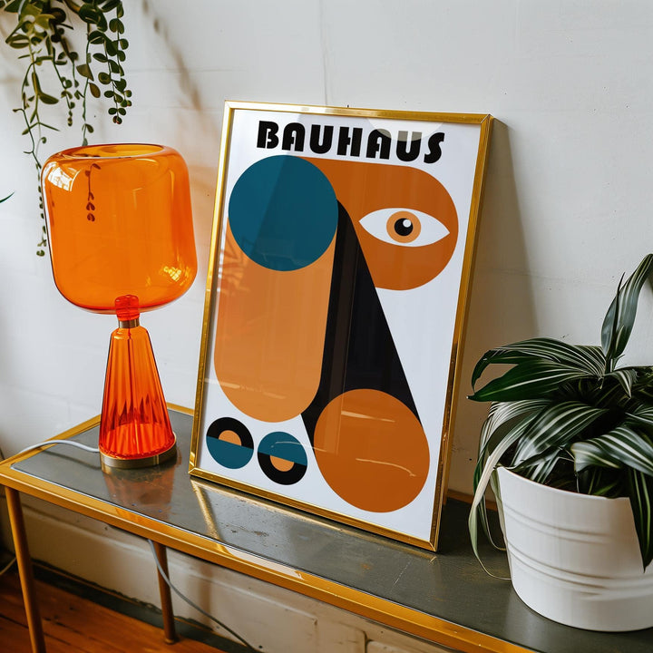 Framed Fun Colorful Print with abstract geometric shapes in orange black and blue on a glass table with an orange lamp and green plant