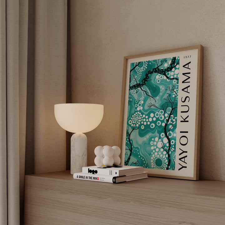 Teal wall decor with abstract branches and dots leaning on a wooden surface beside a lamp