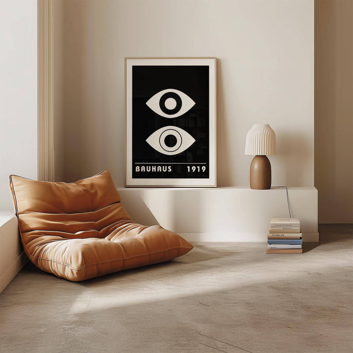 Eye art print in minimalist style with black and white abstract eyes placed on a low white shelf by a brown lamp and chair