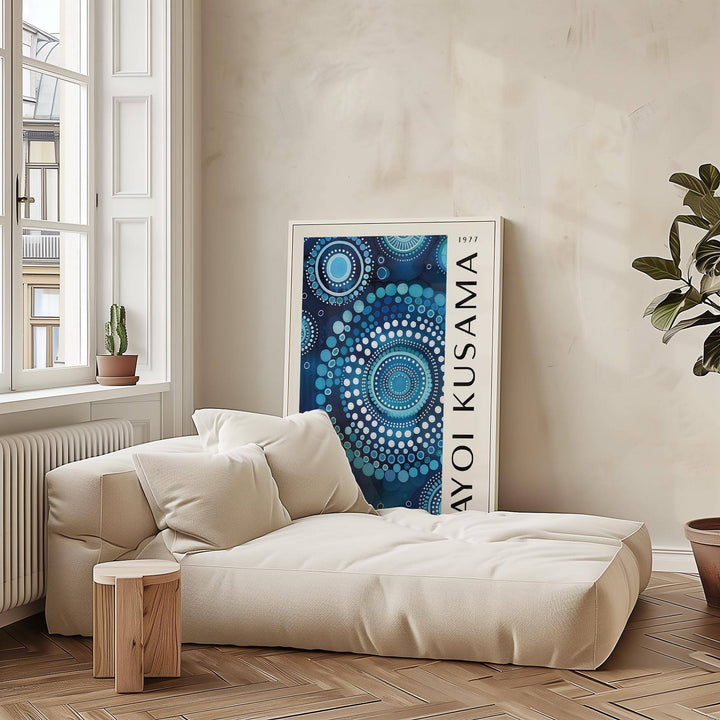 Mandala wall art with blue circular dot pattern leaning on a wall near a beige sofa and tall plant