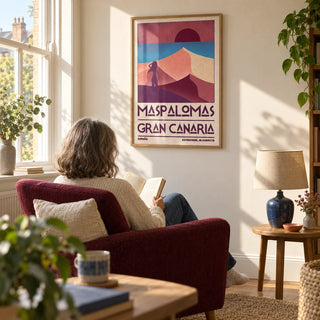 Maspalomas Vintage Wall Art, framed on the wall of a sunlit reading corner in a mature couple's UK flat with a cream plaster wall and a tall window in a living room