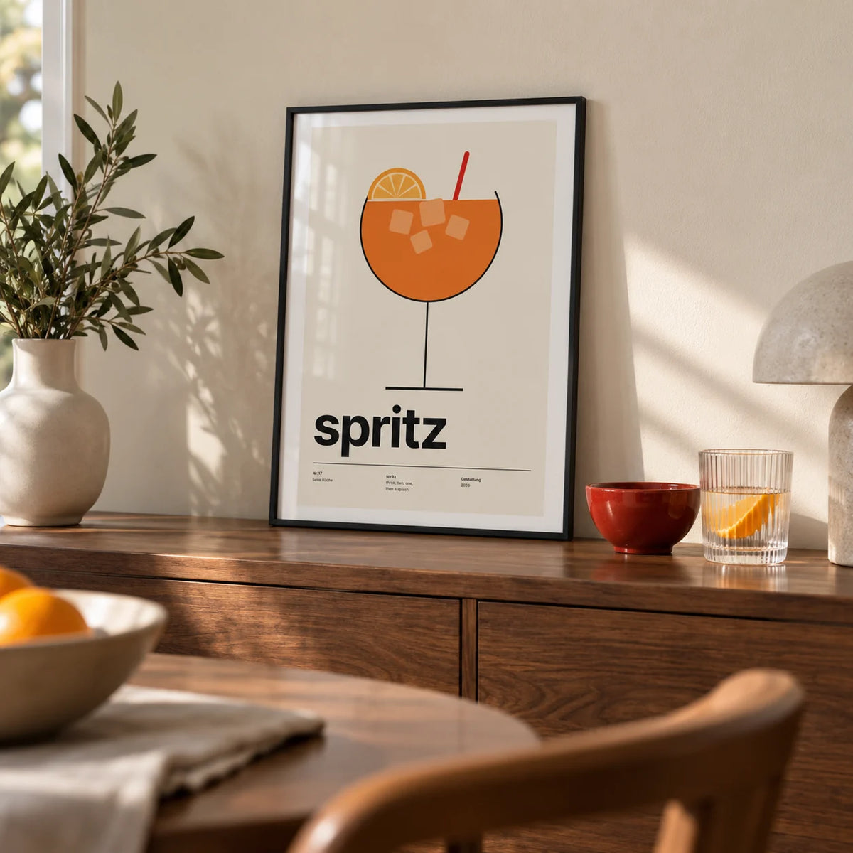 Orange Spritz Print, a small A4 framed print leaning on a walnut sideboard in a dining room