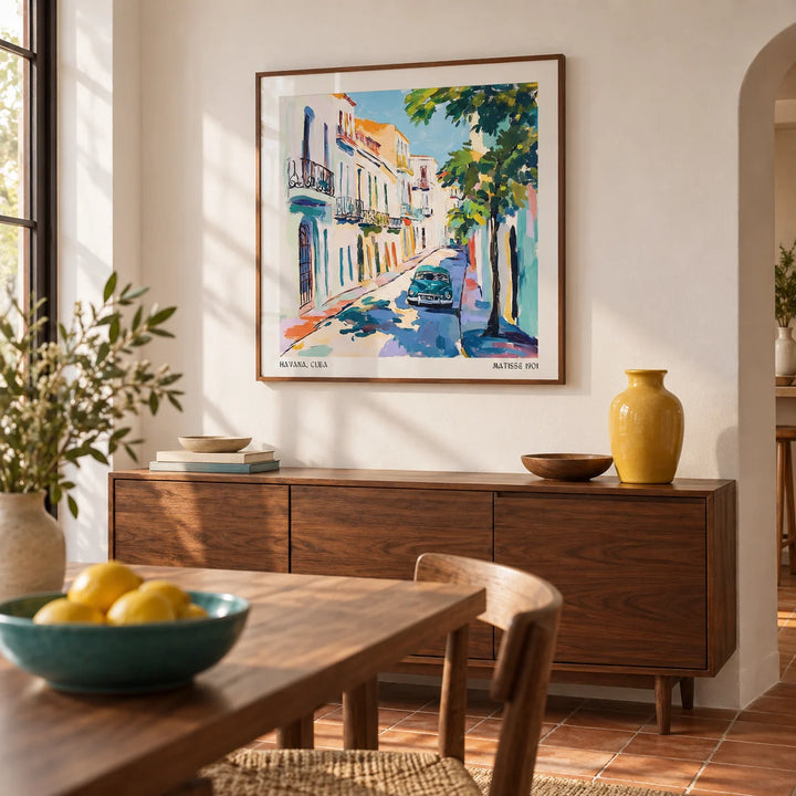 Paintings of Cuba, framed on the wall of a warm dining room with a white wall and a terracotta tiled floor