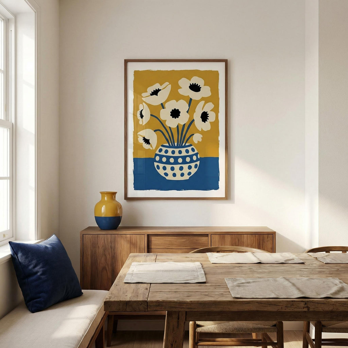 Dining room with wooden table, chairs, and a vase on a shelf. Wall art with flowers in a polka dot vase is displayed.