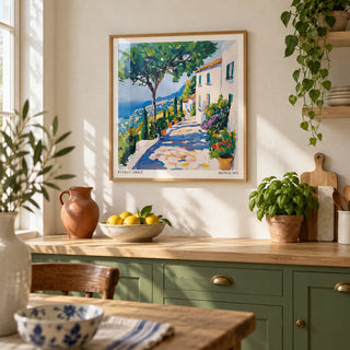 Prints of Amalfi Coast, framed on the wall of a sunny kitchen with a warm white plaster wall and leaf green painted cabinets