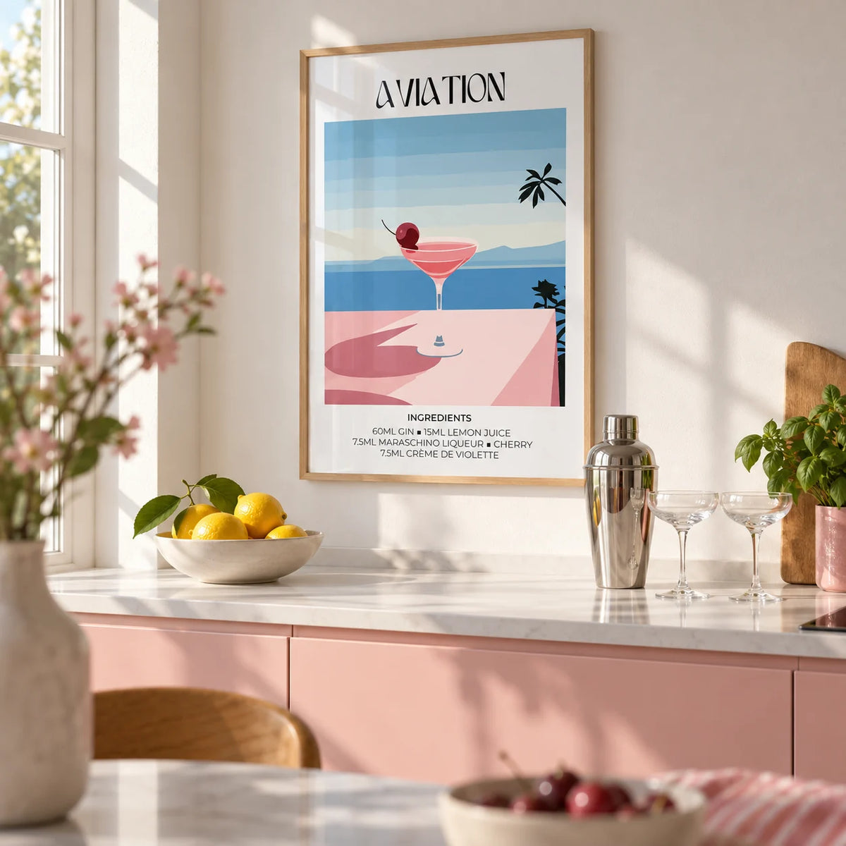 Prints of Cocktails, framed on the wall of a bright kitchen with plain blush pink cabinets and a white worktop