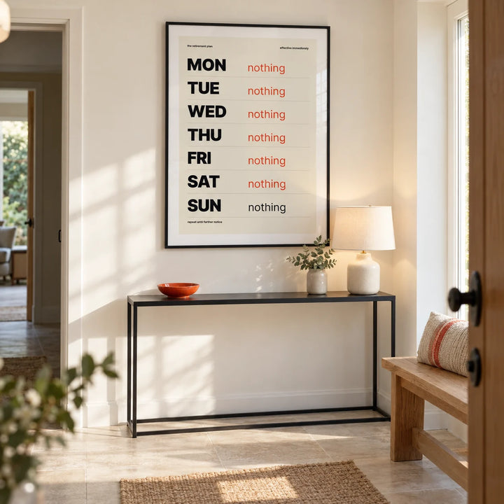 Retirement Plan Print, framed on the wall of a bright modern entrance hall in a retired couple's UK bungalow with a cream wall and pale stone floor