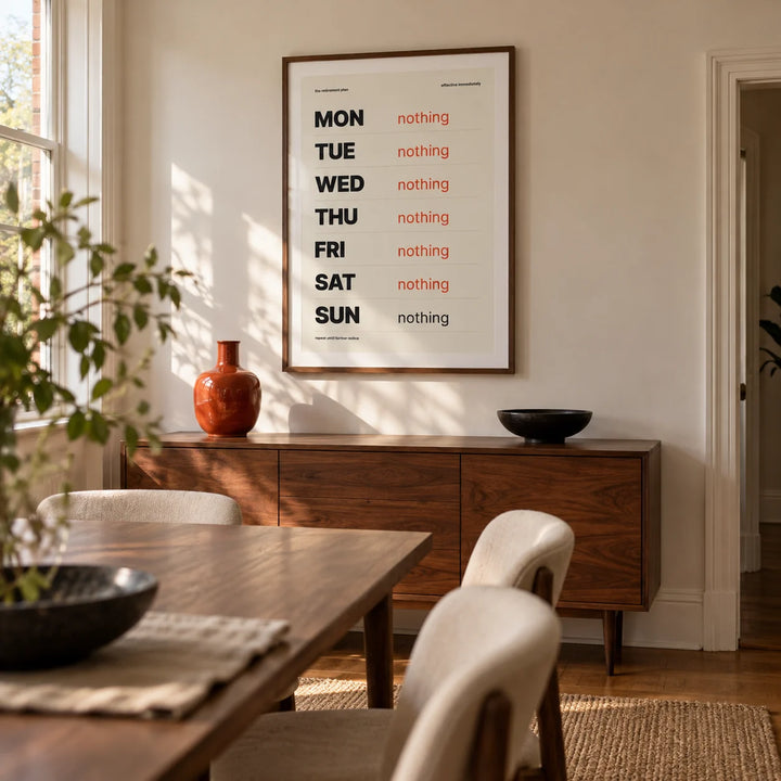 Retirement Plan Print, framed on the wall of a design-led dining room in a UK terraced house with a warm white wall and a walnut dining table