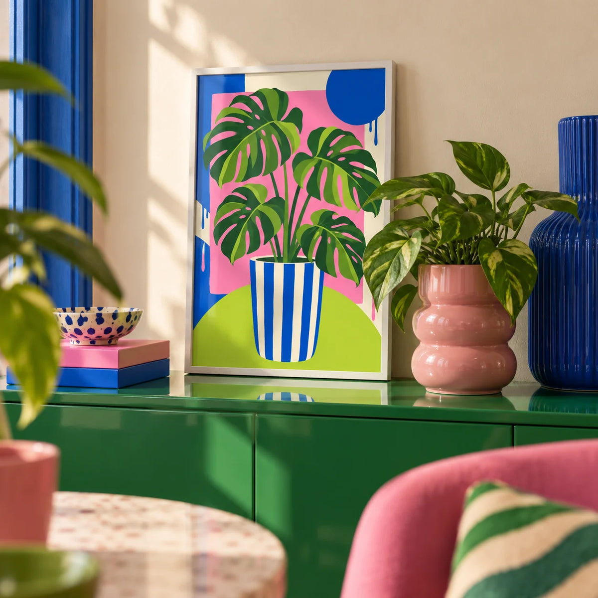 Striped Pot Monstera Print, a small A4 framed print leaning on a colourful lacquered shelf in a living room