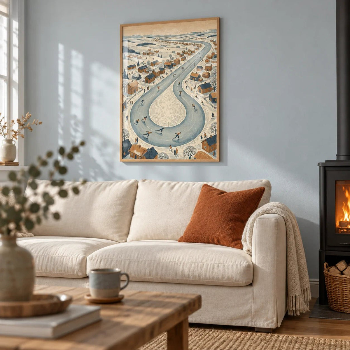 Winter Village Scene, framed on the wall of a cosy living room with an icy pale blue painted wall and a black wood burner
