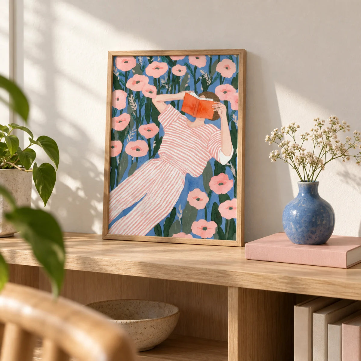 Woman Reading Art Print, a small A4 framed print leaning on a pale oak bookshelf in a living room