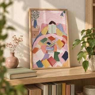 Woman Reading In Bed Art Print, a small A4 framed print leaning on a pale oak bookshelf in a living room