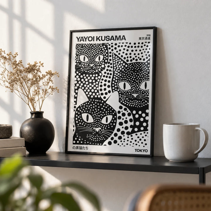 Yayoi Kusama Black Cats, a small A4 framed print leaning on a black metal shelf in a living room