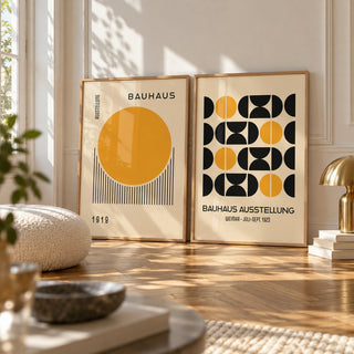Yellow and Black Bauhaus Prints Set of 2 styled leaning on a herringbone floor between a boucle cushion and a brass mushroom lamp: Golden Dawn and Bauhaus Symmetry shown framed side by side (frames not included)