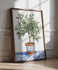 Olive Tree Impression artistique représentant un arbre vert dans un pot en terre cuite avec un motif floral bleu sur un tissu à motifs.