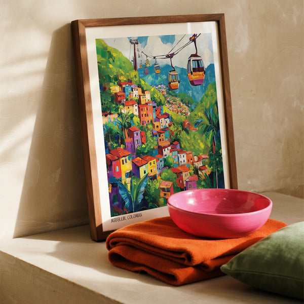 Quadro colorato incorniciato raffigurante Medellin, in Colombia, con funivie appeso alla parete accanto a una ciotola rosa e un panno arancione.